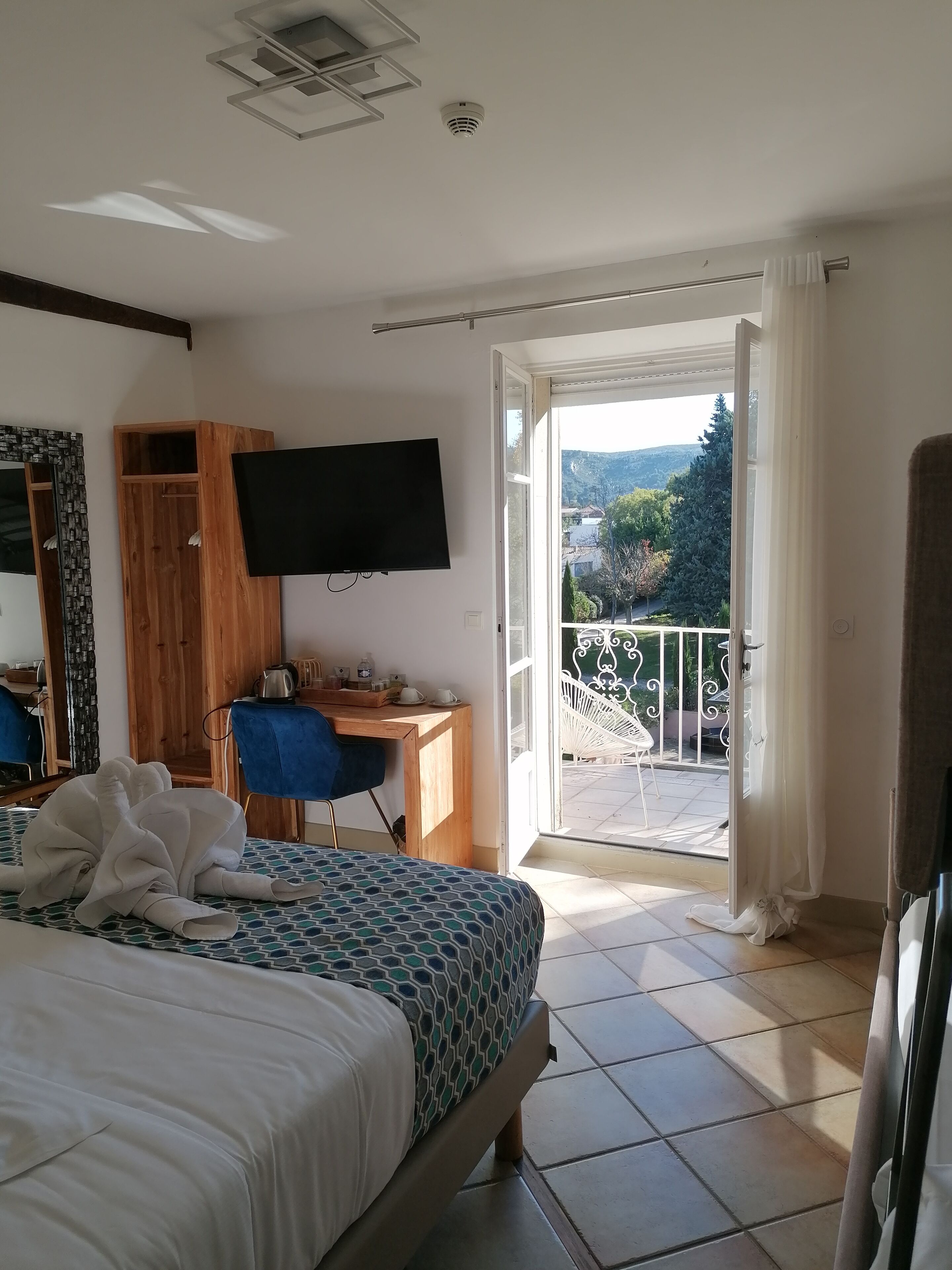 A hotel room with a bed, a desk, a TV, and a balcony with a view of the outdoors.