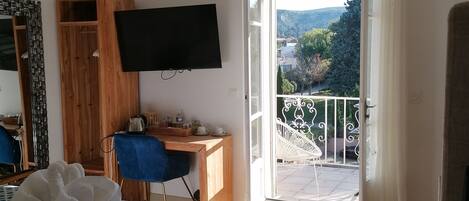 A hotel room with a bed, a desk, a TV, and a balcony with a view of the outdoors.