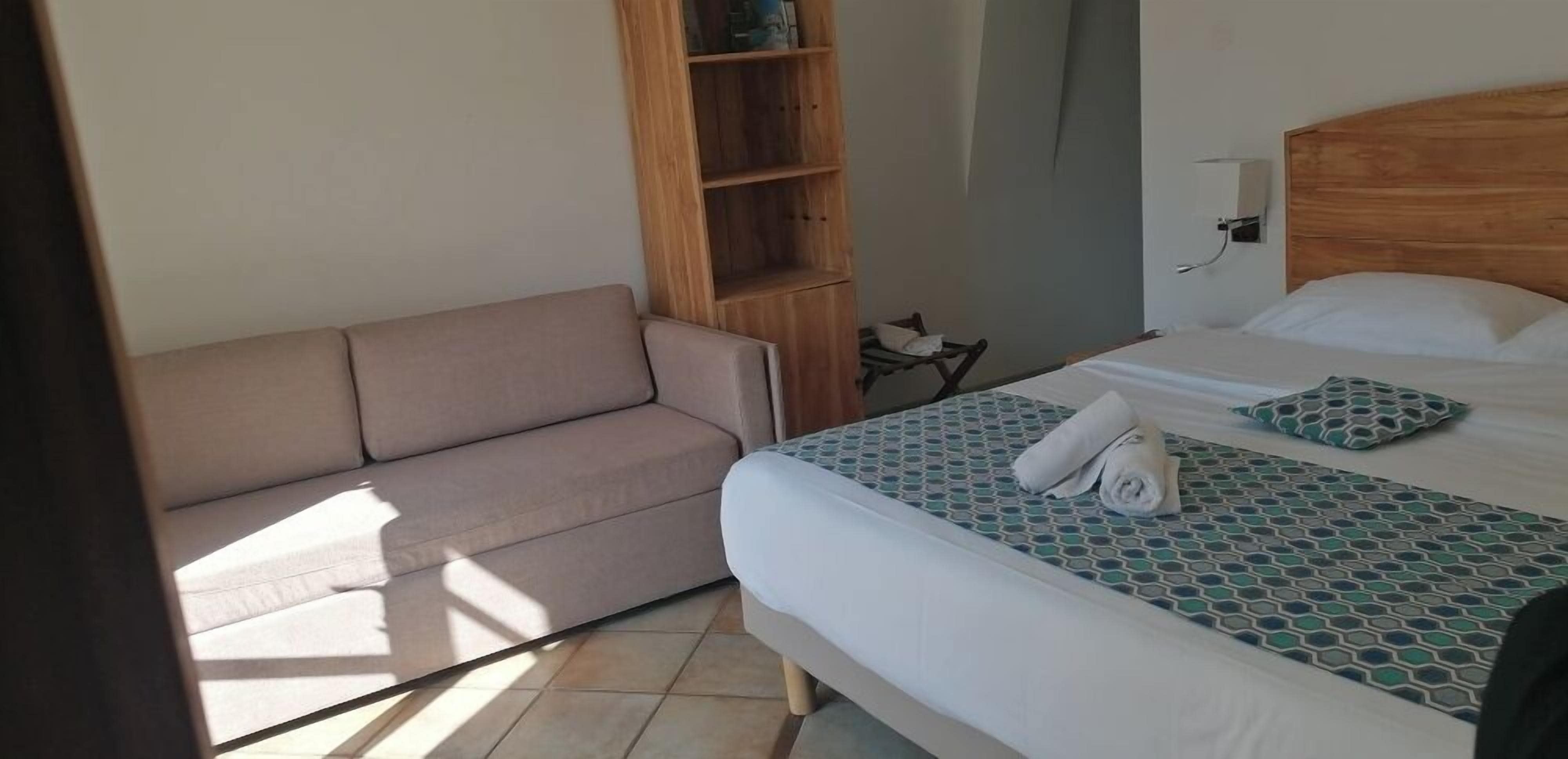 Una camera d'albergo con un letto, un divano e una scaffalatura in legno.
