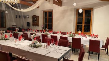 A dining area with multiple tables set for a meal, featuring red chairs and white tablecloths.