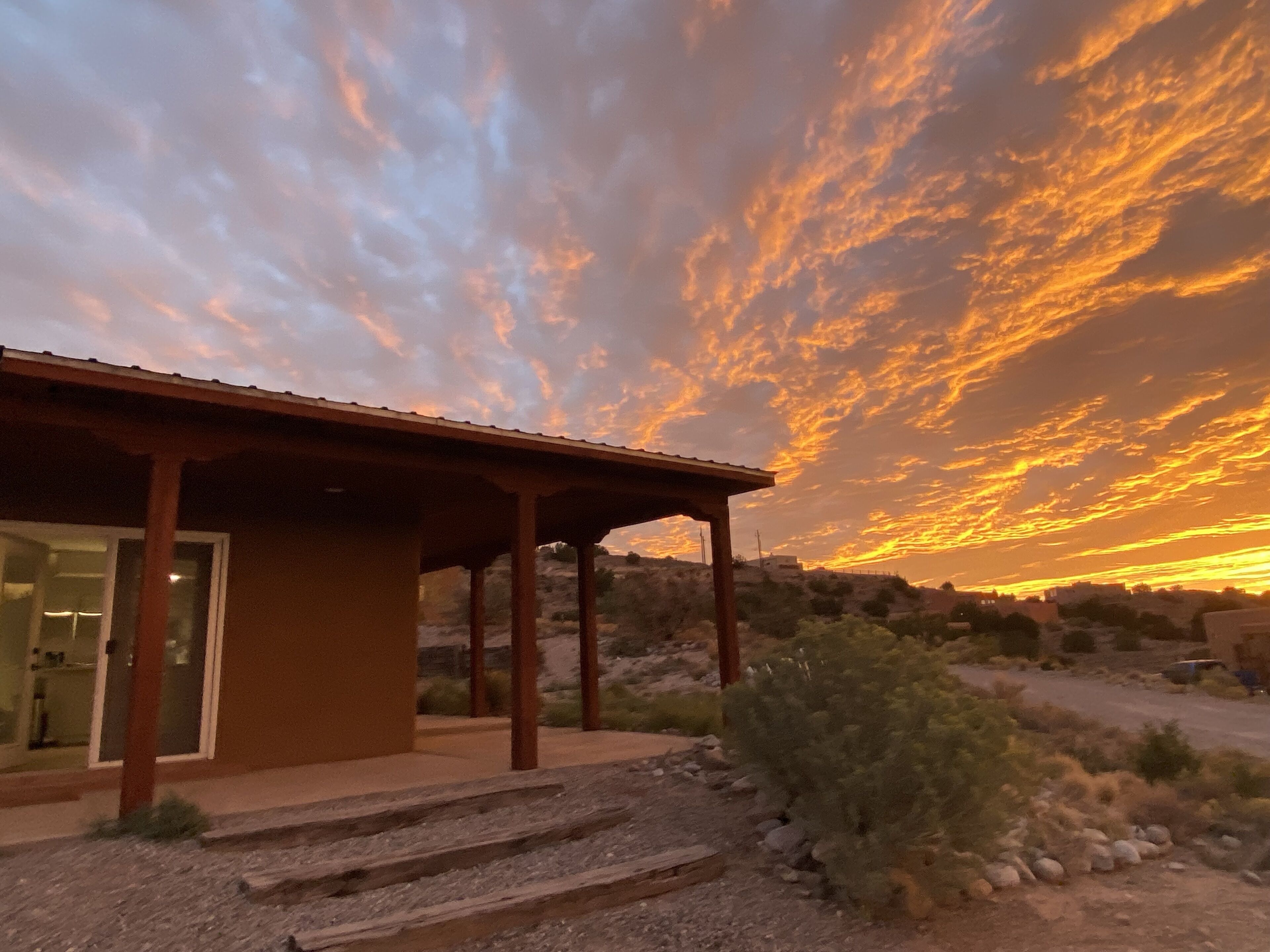 A building with a covered patio area, a stone pathway leading to the entrance, and a desert landscape in the background.