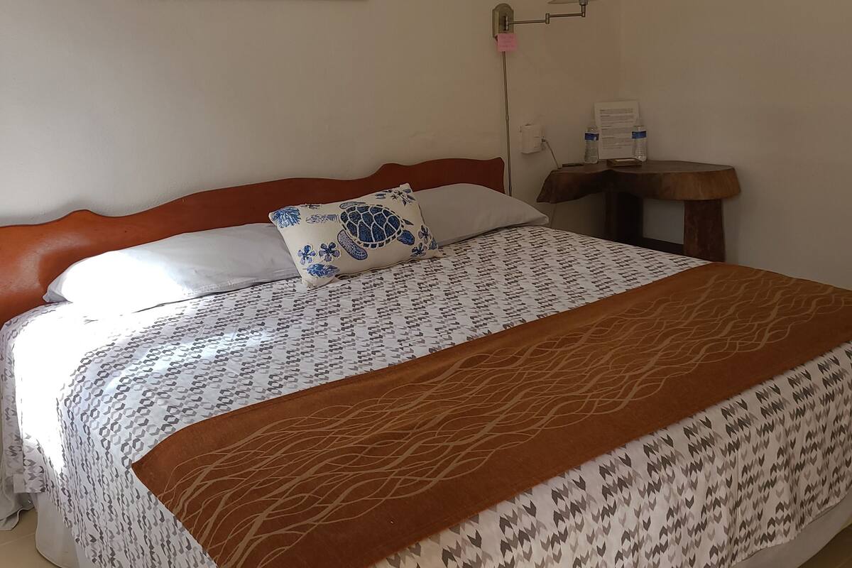 A neatly made bed with a patterned bedspread and a decorative pillow, a bedside table with a lamp, and a wall-mounted artwork.