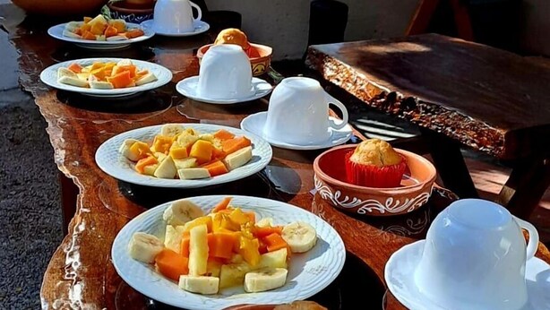 A wooden table set with plates of fruit, white cups, and a clay pot. - Casa Terracota Bacalar (Bacalar)
