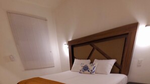 A bedroom with a large bed, a wooden headboard, a bedside table, and a window with blinds. - Casa Terracota Bacalar (Bacalar)