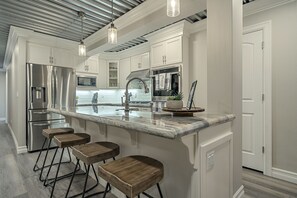 A modern kitchen with stainless steel appliances, a marble countertop, and wooden stools.