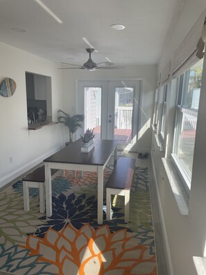 Une cuisine moderne avec un coin repas, un ventilateur de plafond et une vue sur l’extérieur, visible à travers la porte.