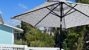 En træterrasse med et hvidt gelænder, et bord med stole, og en stor parasol, der giver skygge.