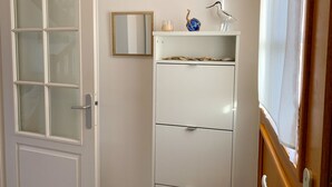 Een kamer met een witte deur met geëtste glazen panelen, een wit kastje met lades, een kleine spiegel, een decoratief vogeltje en een glas met een kaars.