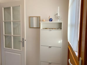 A room with a white door with frosted glass panels, a white cabinet with drawers, a small mirror, a decorative bird figurine, and a glass with a candle.