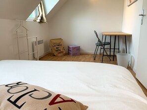Ein kleiner, sauberer Raum mit Bett, Stuhl, Tisch und Heizkörper. Es befinden sich Kartons und ein Kleiderhaken an der Wand.