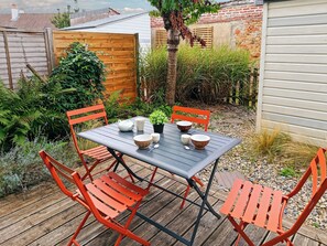A patio with a table set for four, surrounded by red chairs, and a wooden fence in the background.