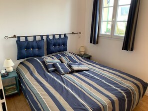A neatly made bed with striped bedding, a bedside table with a lamp, and a window with curtains.