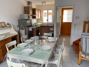 A modern kitchen with wooden cabinets, a built-in microwave, and a dining area set for four with a table covered in a protective sheet.