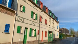Een meerlaags gebouw met een beige gevel, groene luiken en een bord waarop 'Le Clos de L'Abecille' staat.