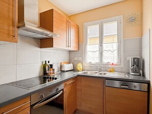 A modern kitchen with wooden cabinets, a stainless steel countertop, a built-in oven, a coffee maker, and a window with blinds.
