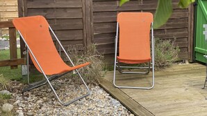 Twee oranje klapstoelen met metalen frames, geplaatst op een houten terras met een houten omheining op de achtergrond.