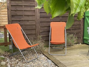 Two orange folding chairs with metal frames, positioned on a wooden deck with a wooden fence in the background.
