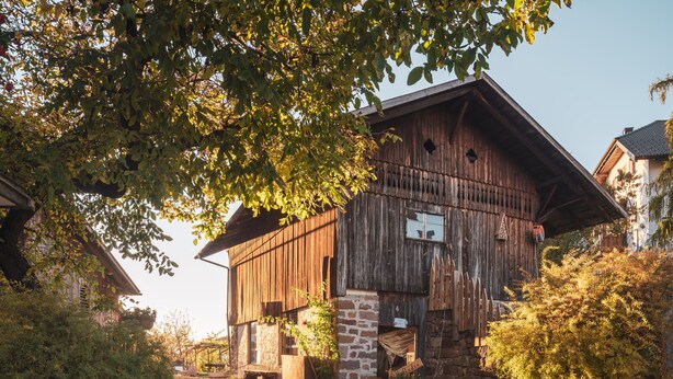 A rustic barn-style building with a stone foundation and wooden walls, surrounded by greenery and a gravel path. - Traditional vacation apartment in rustic style with view of the Schlern (Völs am Schlern)