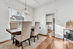 A dining area with a wooden table and four chairs, a hanging light fixture, and a view into the kitchen.