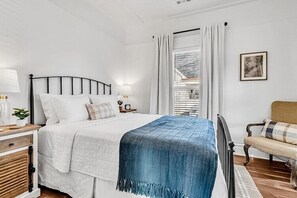 A bedroom with a bed, bedside table, lamp, and a view of a balcony.