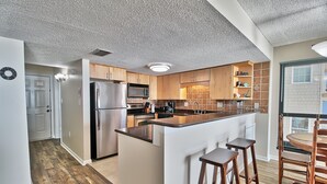 Een moderne keuken met een centraal eiland, houten kasten, roestvrijstalen apparatuur en een eethoek met een ronde tafel en barkrukken.