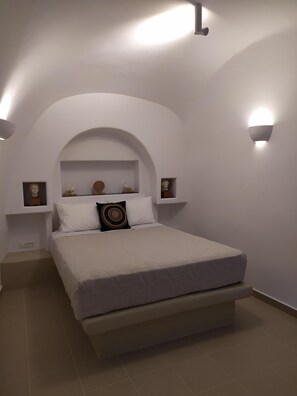 A bedroom with a bed, white walls, an arched alcove, and wall-mounted light fixtures.