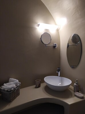 A bathroom with a round mirror, a white sink, and a towel basket.