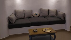 A modern living room with a dark-colored sofa, a small wooden coffee table, and two wall-mounted lights. - Santorini Cave Suite (Thera)