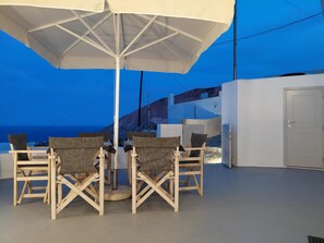 Une terrasse avec une table et quatre chaises, protégée par un grand parasol, d’où l’on peut admirer un paysage côtier.