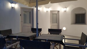 A dining area with tables and chairs, a ceiling fan, and wall-mounted lights. - Santorini Cave Suite (Thera)