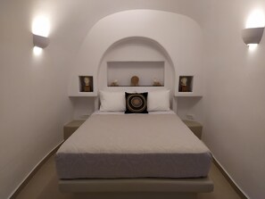 Une chambre à coucher au style minimaliste, avec un grand lit, des murs blancs et deux lampes fixées au mur.