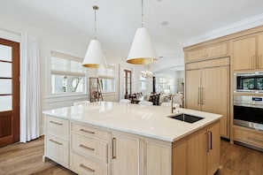 A kitchen with a large island, wooden cabinets, stainless steel appliances, and pendant lighting.