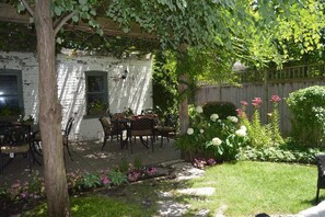 Un espace extérieur aménagé en terrasse, avec une table et des chaises, entouré d’un jardin où poussent différentes plantes et fleurs.