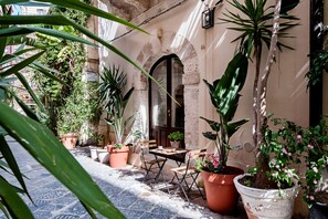 An outdoor seating area with a table and chairs, surrounded by potted plants and a stone wall.