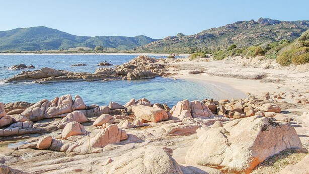 A rocky beach with clear blue water and distant mountains. - Beautiful apartment in Villaputzu CA (Villaputzu CA)
