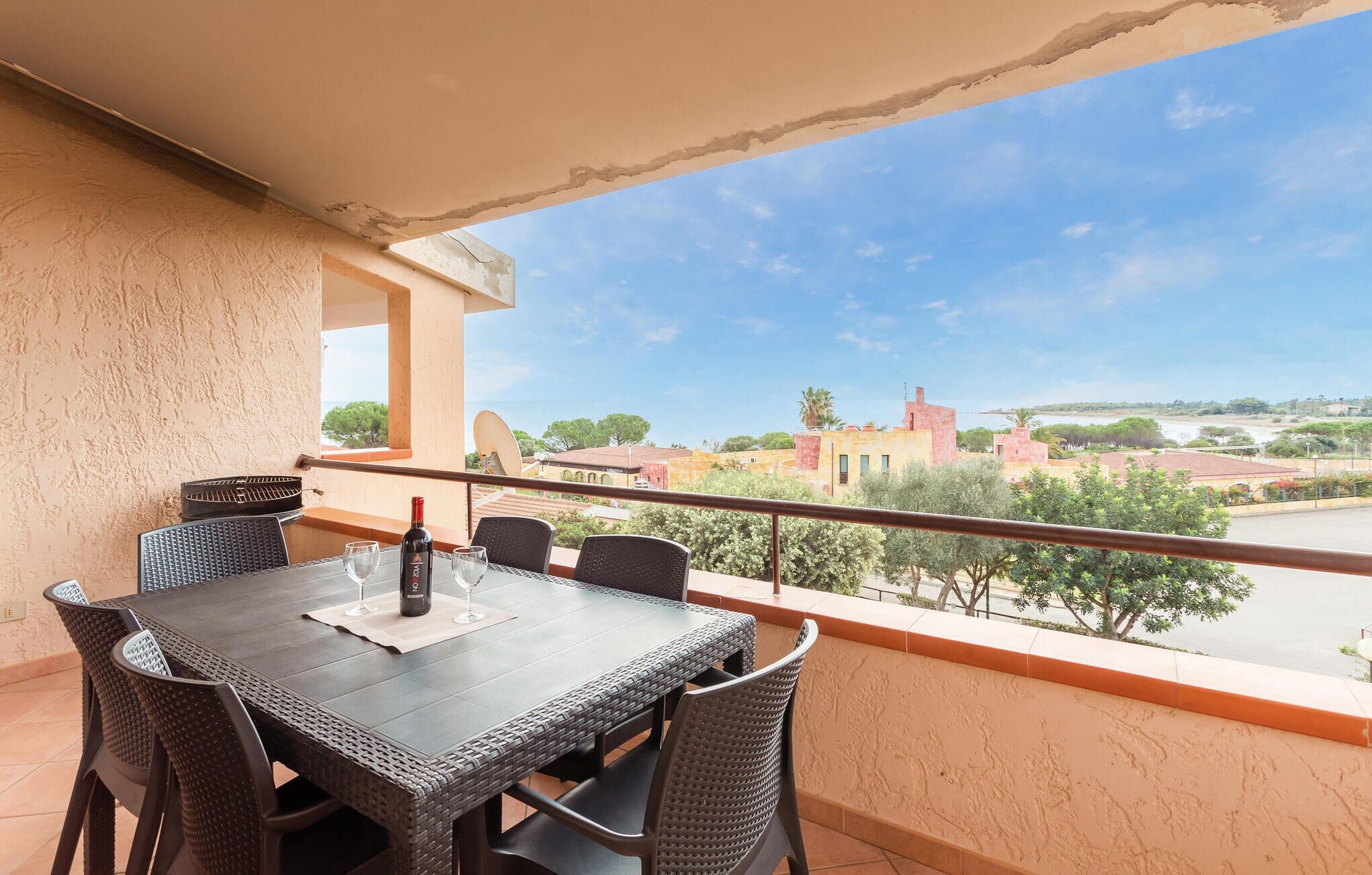 A balcony with a table and chairs, a bottle of wine, and a view of buildings and trees.
