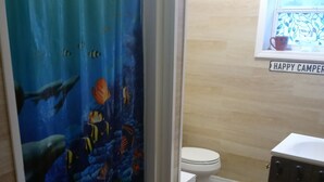 A bathroom with a shower curtain depicting underwater scenes, a toilet, a sink, and a window with a view of the outdoors.