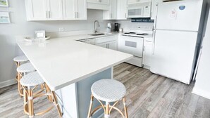 Een moderne keuken met witte kasten, een centraal eiland met barstoelen, een ingebouwde magnetron en een koelkast.