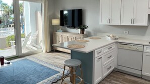 Een moderne keuken met witte kasten, een centraal eiland met krukken, een ingebouwde televisie en een groot raam met uitzicht op palmbomen.