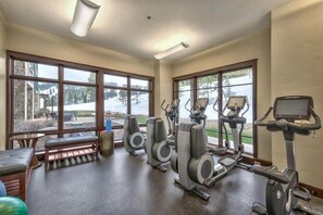Une salle de sport équipée de vélos d’appartement, de tapis de course et d’un appareil elliptique. De grandes fenêtres offrent une vue sur un espace extérieur enneigé.