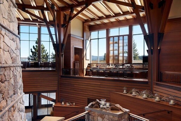 Un bar spacieux avec de hauts plafonds, des poutres en bois, de grandes fenêtres et un mur en pierre.