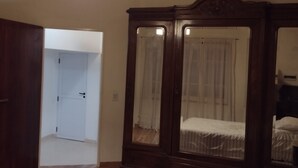 Un dormitori amb un armari de fusta, un llit amb edredó floral i una làmpada penjant.