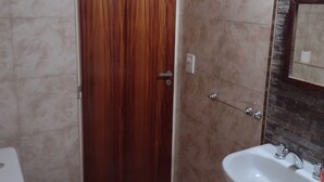 Un bany amb una porta de fusta, un vàter blanc i un lavabo blanc amb un mirall a la part superior.