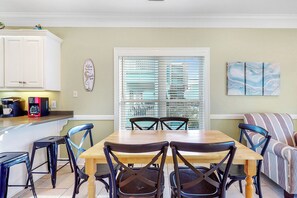 Un coin repas avec une table et des chaises en bois, une cuisine avec des placards blancs, une machine à café et un panneau décoratif accroché au mur.