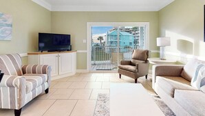 A living room with a television, two sofas, a coffee table, and a balcony with a view of a blue building. - OGP3AB. Great 6BR. Sleeps 20. Community Dock. Beach. Pool. Tremendous value! (Gulf Shores)