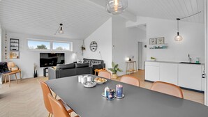 Moderni keittiö, jossa on ruokailutila. Tilaan kuuluu suuri ruokapöytä, jossa on kynttilöitä, sohva ja televisio.