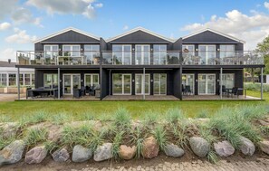 Ein modernes, dreistöckiges Haus mit großen Fenstern, einem Balkon und Sitzgelegenheiten im Freien.
