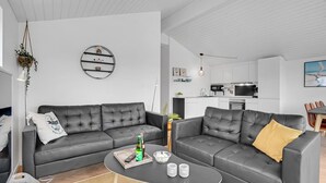 Moderni olohuone, jossa on harmaa sohva, sohvapöytä ja taustalla näkyy keittiö.