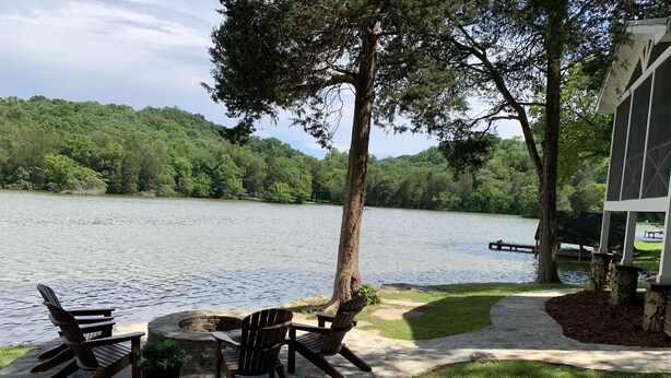 A lakeside patio with Adirondack chairs and a table, surrounded by stone pillars and a grassy area. - Bluebird Rest - Peaceful Lake Retreat (Kelso)