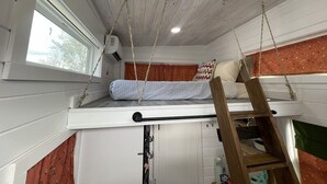Ett litet rum med en våningssäng, en liten stege, ett fönster och en takfläkt.